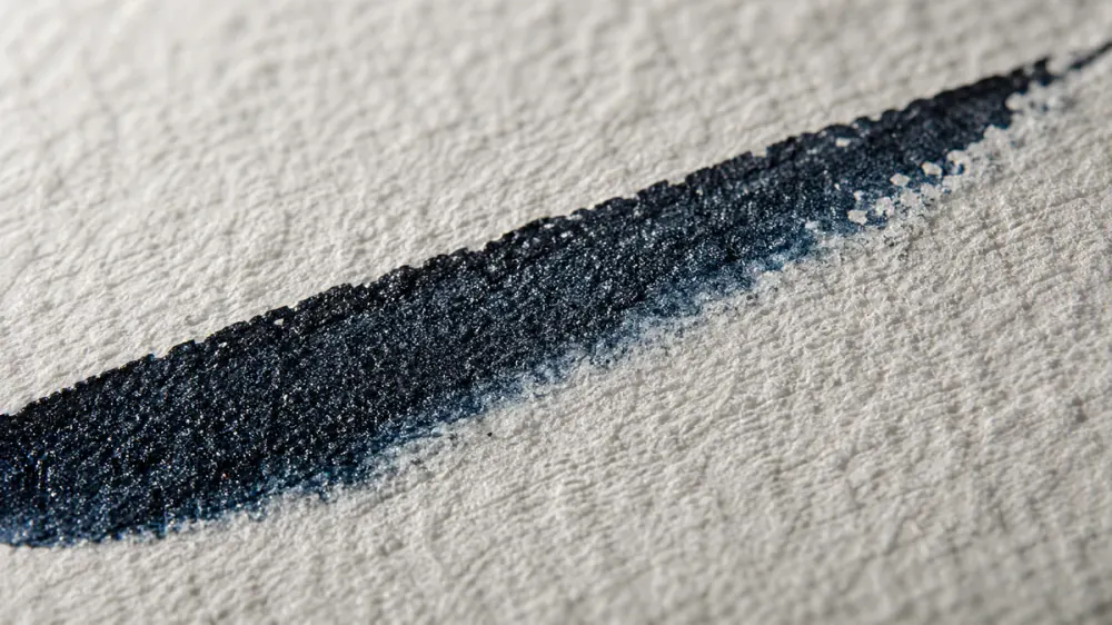 Extreme macro of textured cotton watercolor paper with a single fresh ink stroke bleeding into the fibers