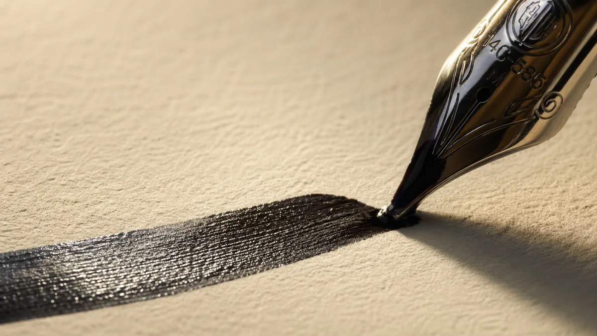 Macro of a fountain pen italic nib laying down a wet, glossy shaded stroke on cream paper