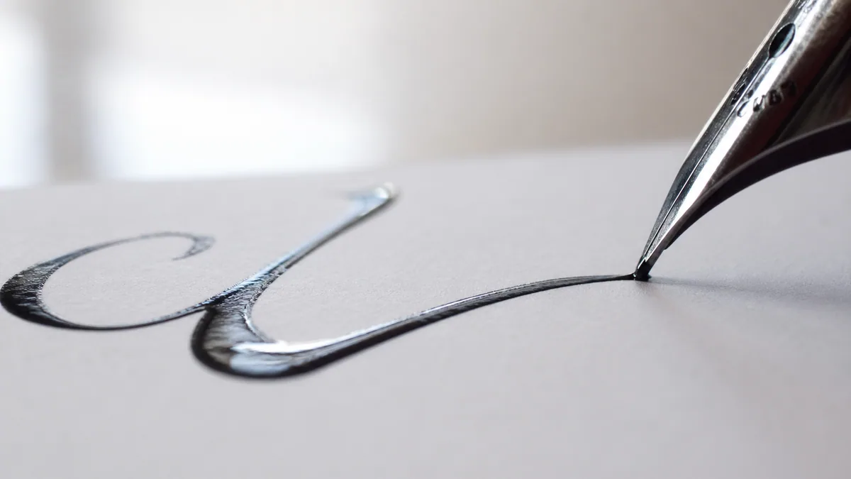 Macro of a freshly inked compound-curve stroke flowing across smooth white paper, nib still touching the page