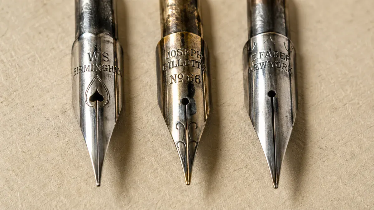 Extreme macro of three pointed calligraphy nibs side by side — Nikko G, Hunt 101, and Gillott 303 — on textured paper